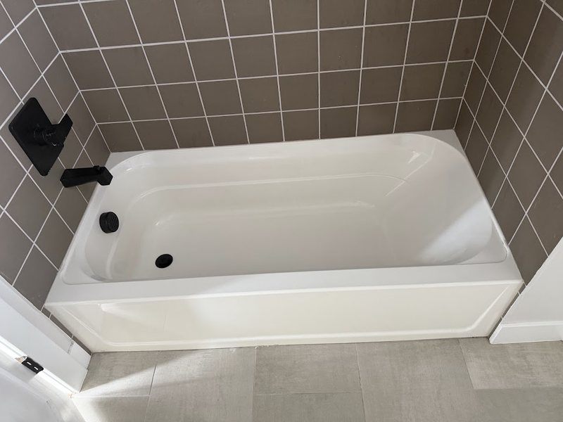 Apartment bathroom with a white bathtub, tiled surround and black fixtures.