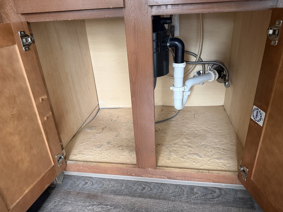 Under-sink kitchen cabinet with a worn, uneven base before repair.